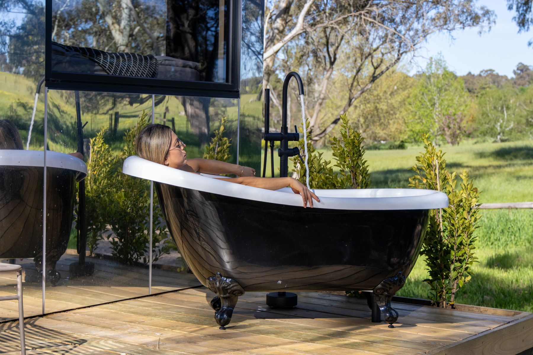 A freestanding bath framed by a wall of bushland glass