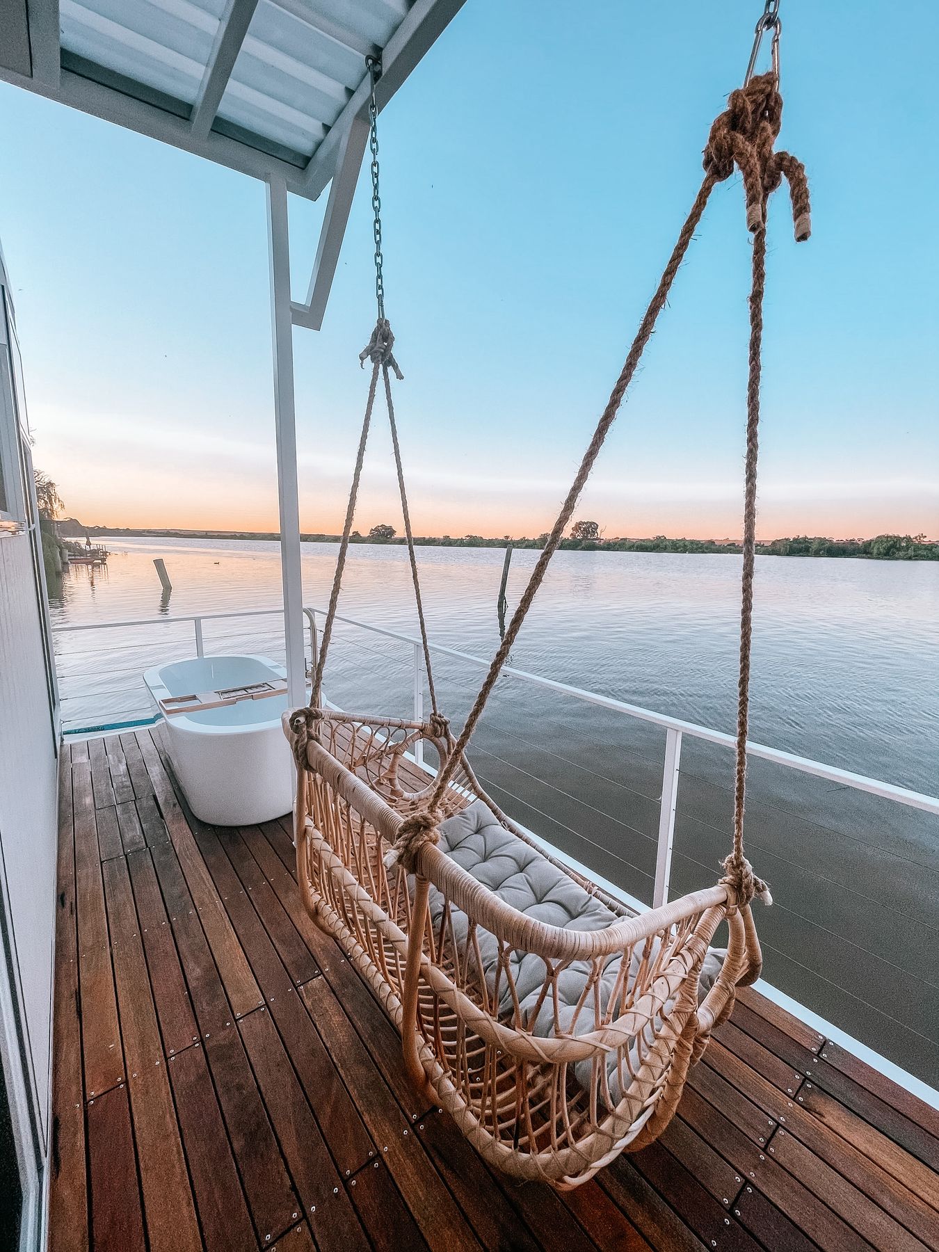A hanging chair on a deck over the water at sunset